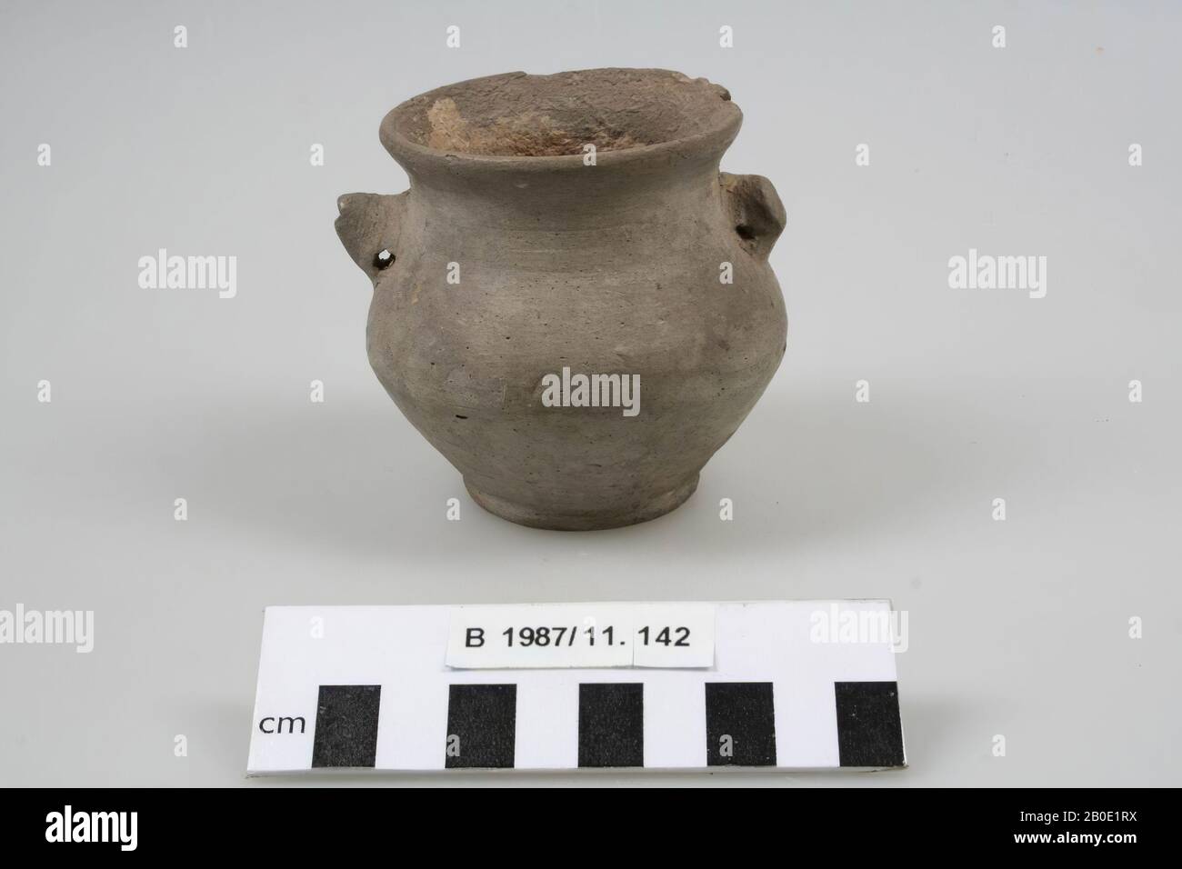 An earthenware pot with a disk base. The wall slopes diagonally upwards to a round bend. Above the bend, the wall slopes inwardly upwards to a short wide neck with an outwardly curved and rounded edge. Two lobe handles are placed on the shoulders. The pot is light gray polished., Crockery, earthenware, H 7.8 cm, D 8.2 cm, D edge 7 cm, Iron Age 1200-600 BC, Iran Stock Photo
