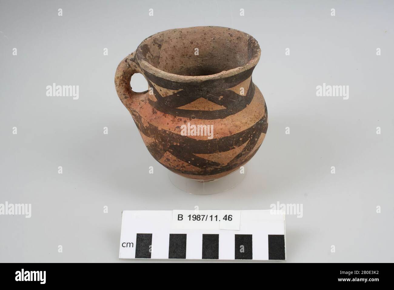 An earthenware cup with a foot and an oval body that goes through a round  bend in a high, concave neck. The edge is outwards and is finished  undiluted and irregular. A