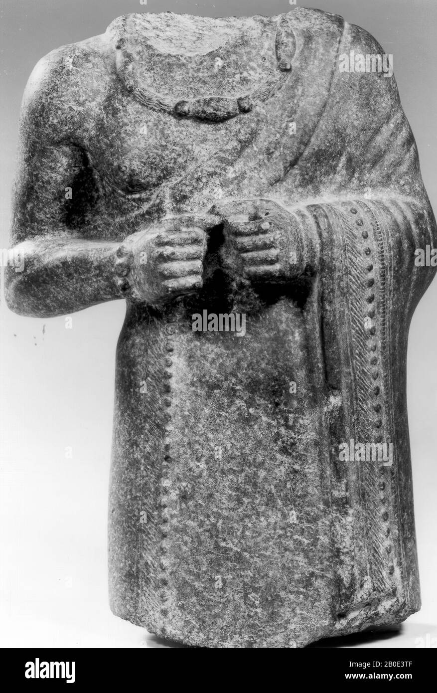 A fragment of an image. Probably it is a man dressed in a cloak hanging over the shoulder with richly decorated piping. He wears wide bracelets and around his neck hangs a composite necklace with convex beads and a large pendant. Very cleverly the sculptor has been able to capture the mantle folds and the muscle parts in the extremely hard material. The statue probably represents a prince of Eshnunna., Sculpture, stone, basalt, diorite, H 27 cm (10 5 Stock Photo