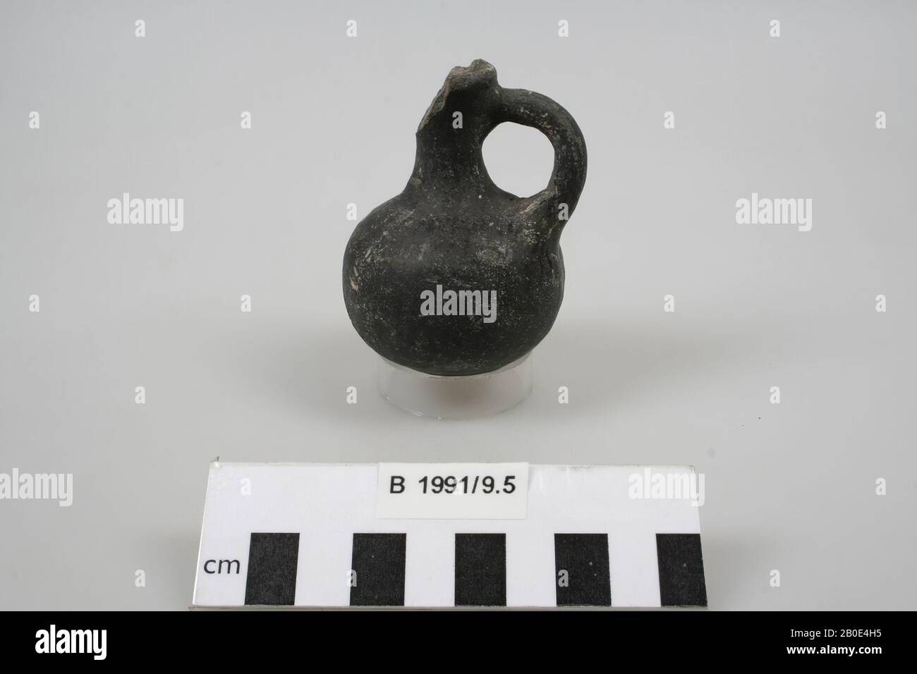 Miniature jug of baked clay. The bottom is convex and runs downwards sharply. The body is bulging. The neck is narrow and high and runs concave upwards (inside neck diameter: 0.9 cm). The edge is outwards and is slanted and rounded. A large part of the rim and the neck is missing. Manufactured on the wheel. The clay is light brown in color, has a fine texture and is agglutinated with lime and fine sand. The surface is dark gray in color and is vertically polished on the outside. On a part of the bottom and on the wall the surface is completely weathered and flakes are missing. Elsewhere white Stock Photo