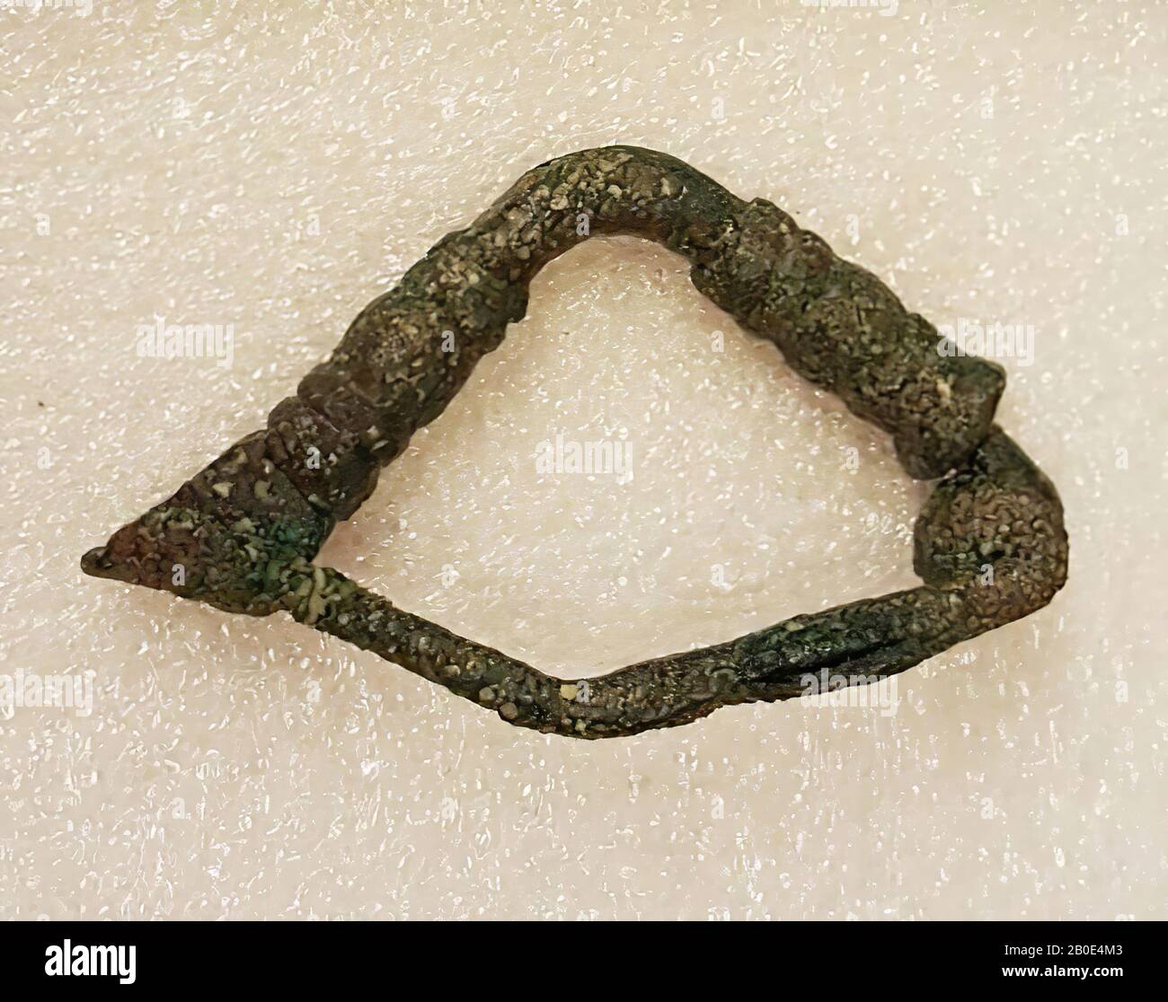 A bronze fibula. The arch is angled outwards in the middle. On both sides of the curve a broad and long thickening, over the width decorated with several grooves (diameter arc: 0.3 cm, thickenings: 0.6 cm). One end of the arch forms a locking hook. The hook consists of a flat part with the end bent round backwards and decorated along the length with four parallel grooves. The shape and decoration of the bow and hook are reminiscent of a hand and an arm decorated with bracelets. The other end of the arch is spirally bent and merges into an angled outwardly bent needle (diameter: 0.2 cm Stock Photo