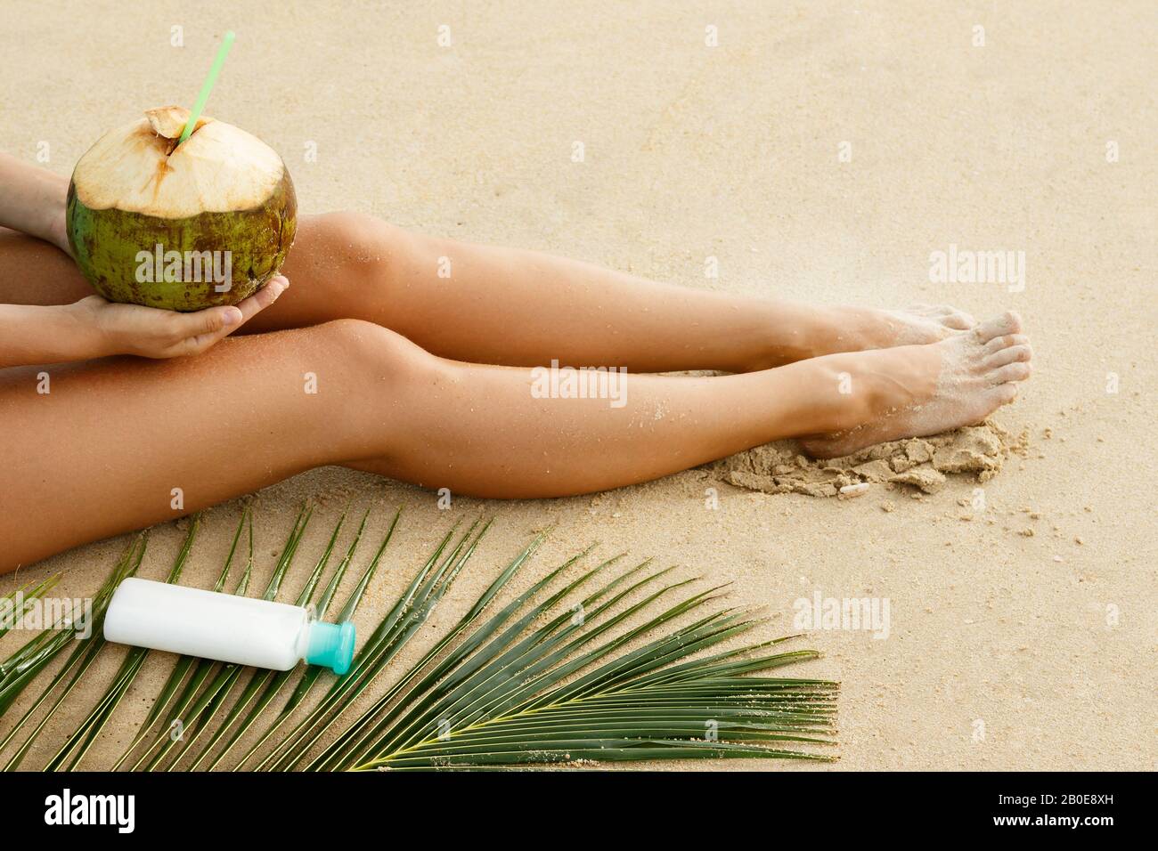 Relaxing on the beach. Female legs, coconut and sunblock lotion. Stock Photo