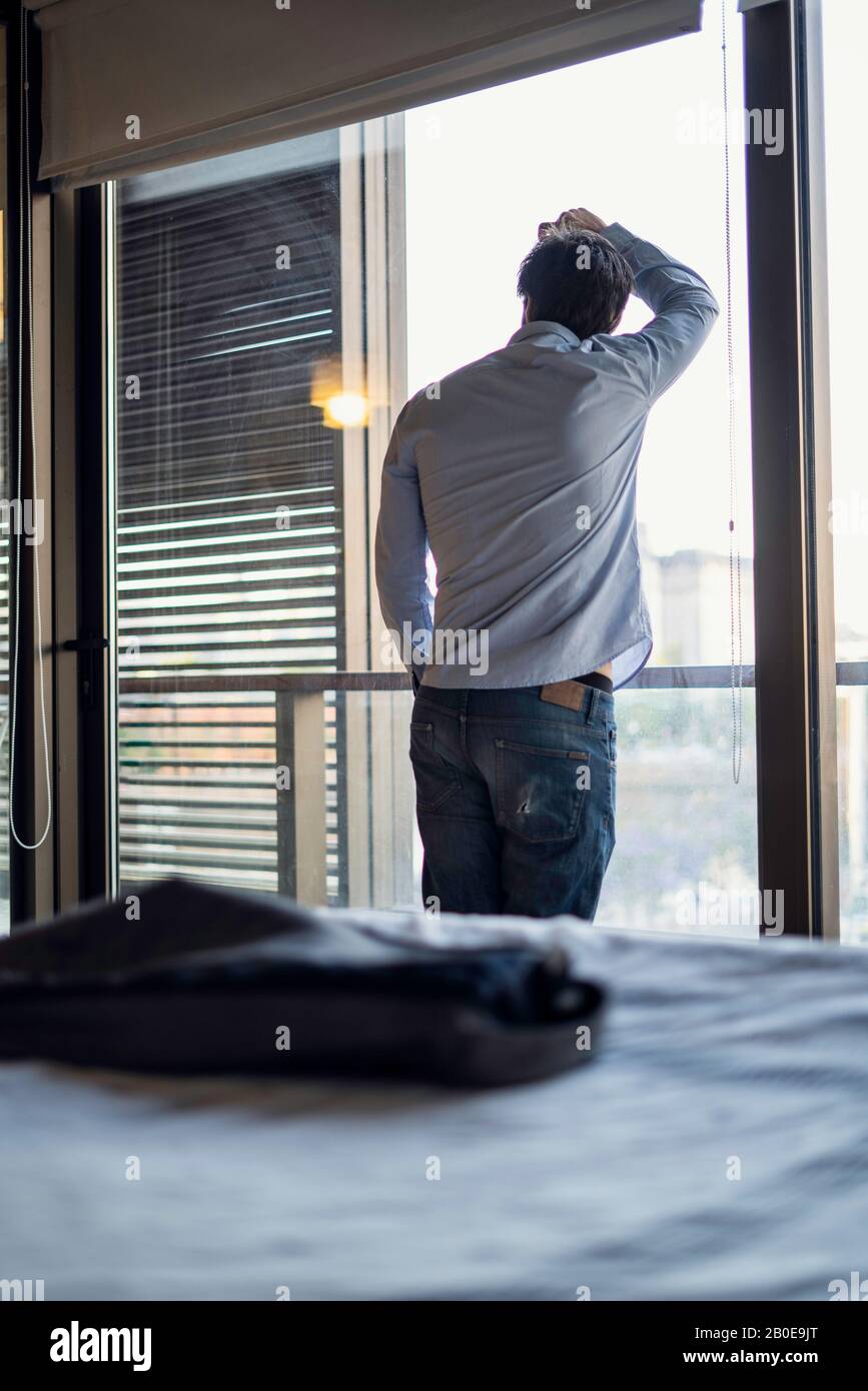Thoughtful young man standing by the window Stock Photo