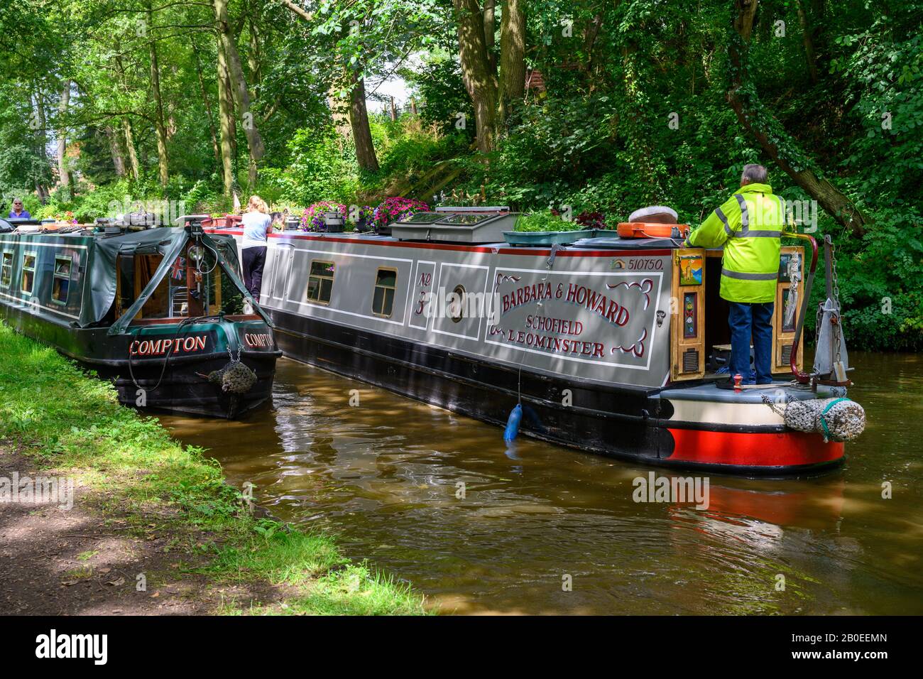Man on narrowboat tries to manoeuvre past a moored boat on the Shropshire Union Canal near Gnosall in Staffordshire. Stock Photo