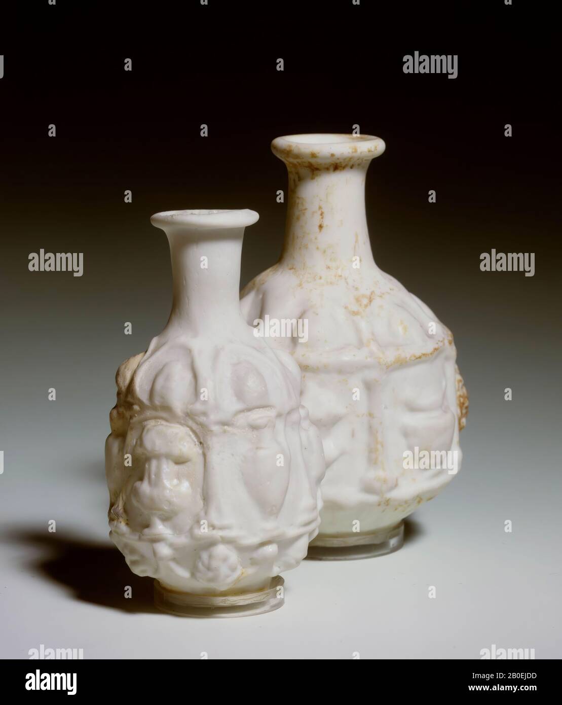 White glass bottle decorated with relief work. The belly is hexagonal cylindrical. The six compartments are bounded by columns and decorated with different forms of vases and two bunches of grapes. Blown into shape. From the tombs of Phocea, vial, glass, 8.2 cm, I, Turkey Stock Photo