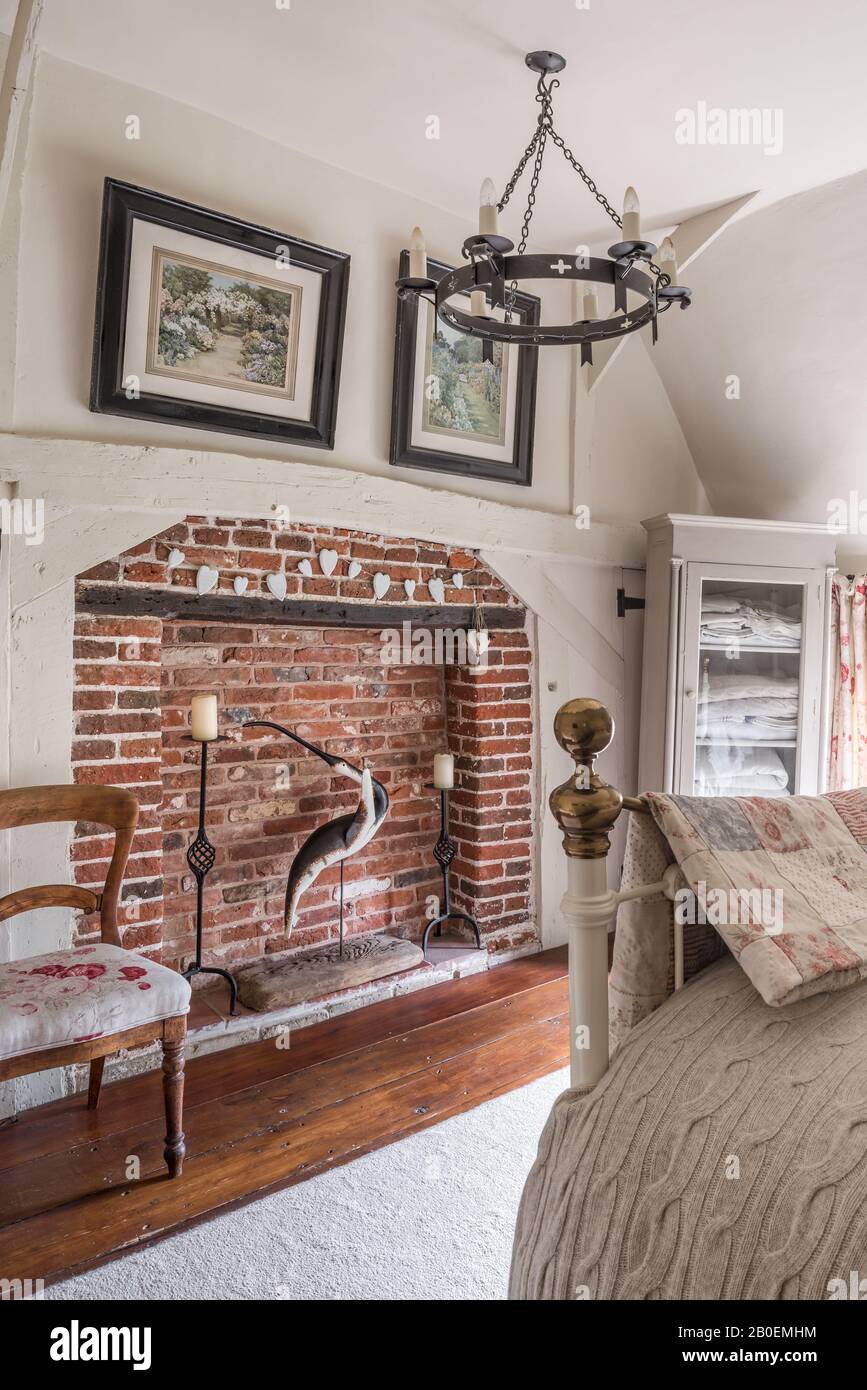 Red-brick fireplace with antique chair upholstered in Kate Forman’s Red Roses. Stock Photo