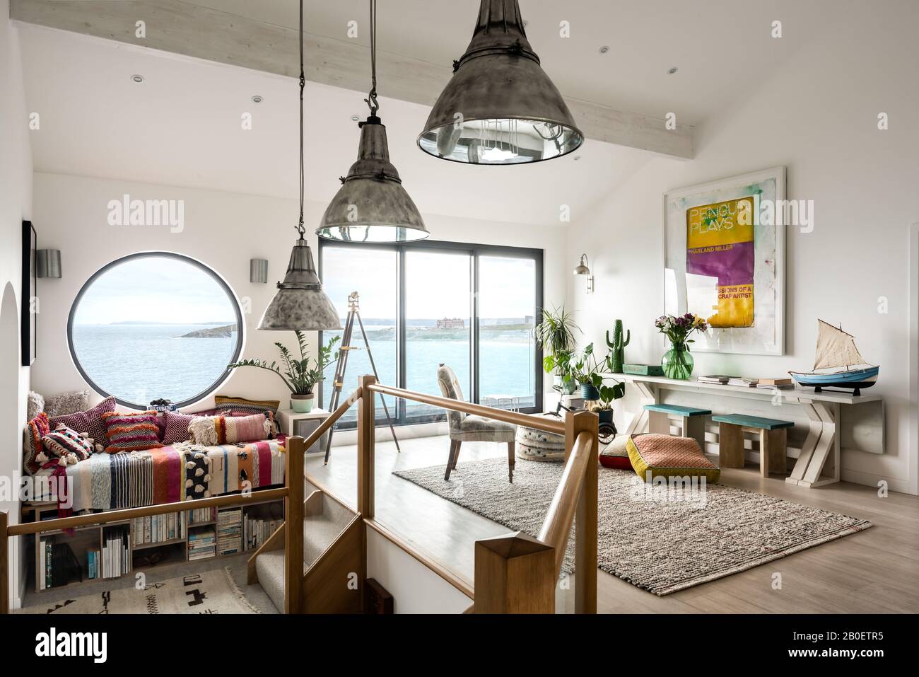Reclaimed lights and large porthole window in split level 1960s renovation with view to Fistral Beach Stock Photo