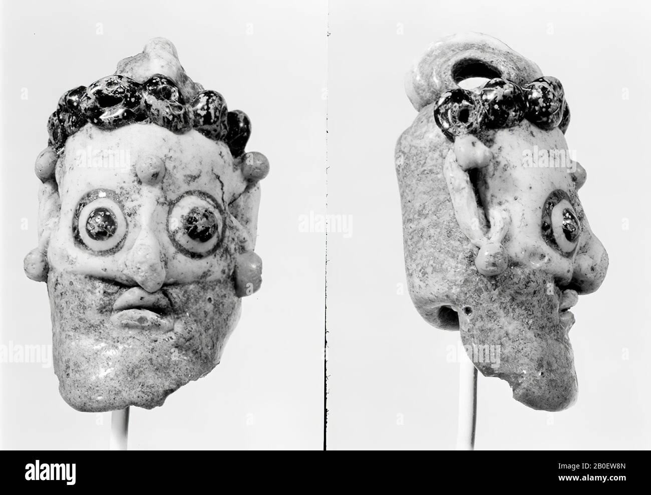 mask, Carthaginian face of white and light blue glass, details applied with dark blue. White face with a nose nose, ears, hair and beard of turquoise glass. On the forehead are six blue balls and in the middle of the forehead is a yellow dot. Earrings of yellow glass are placed above and below both ears. Large convex eyes that are delineated with dark blue, the yellow lips are attached separately., Amulet, person, glass, sand core method, 2.1 x 1.3 x 3.4 cm, Greco-Roman Period 5th-3rd Century BC, Egypt Stock Photo