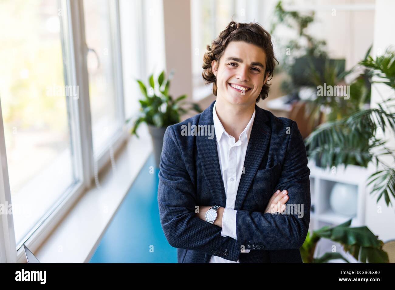 Portrait of an elegant young businessman standing with arms crossed in ...