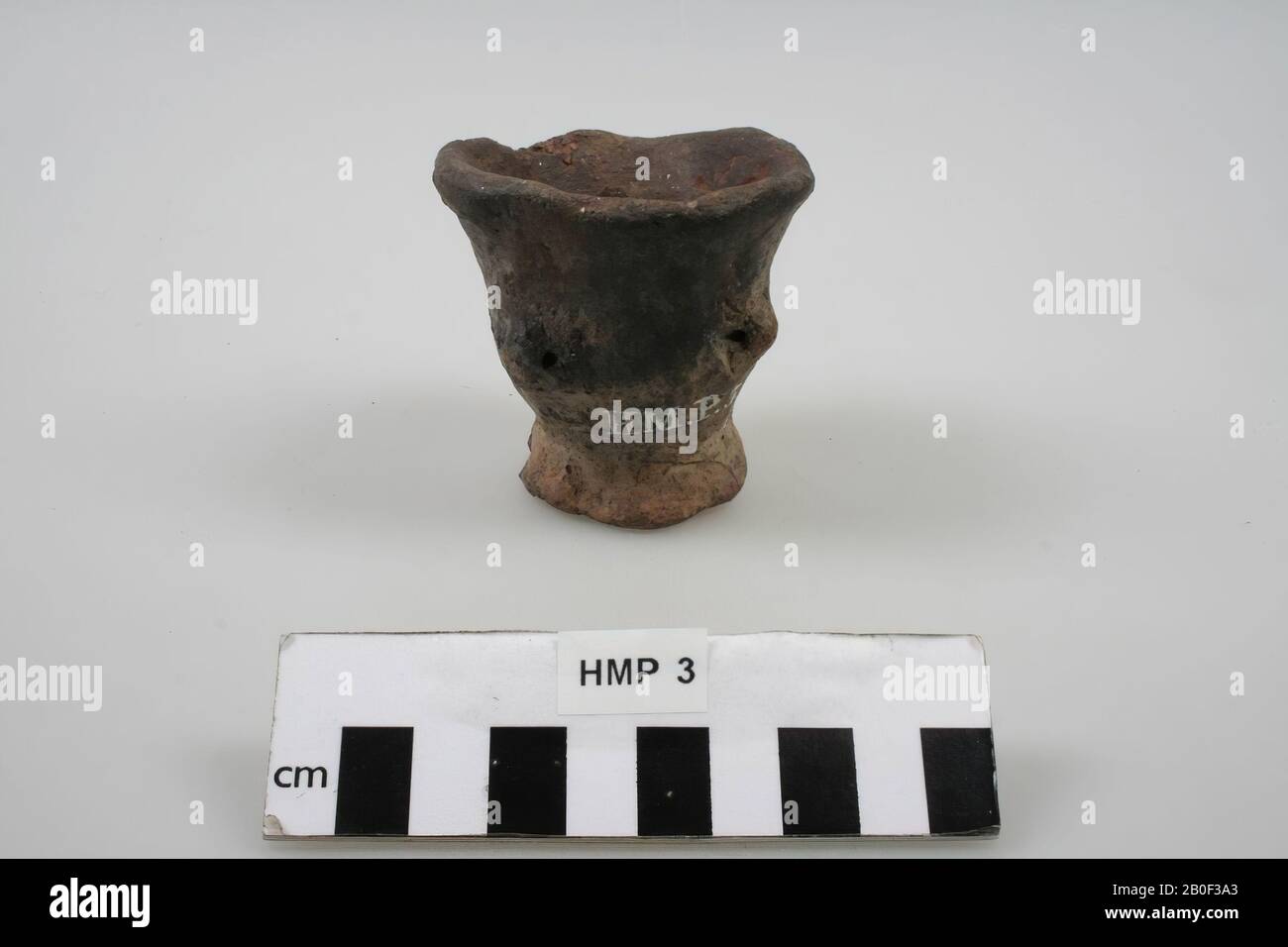 Pot with three small ears, cup-shaped, made of hand-formed earthenware. The red color comes from the red earth that a shipper's wife kept in it. Piece of the rim is missing, parts of the foot are missing, pot, earthenware (hand shaped), h: 6.5 cm, diam: 6.5 cm, roman, Netherlands, Friesland, Leeuwarderadeel, Hijum Stock Photo