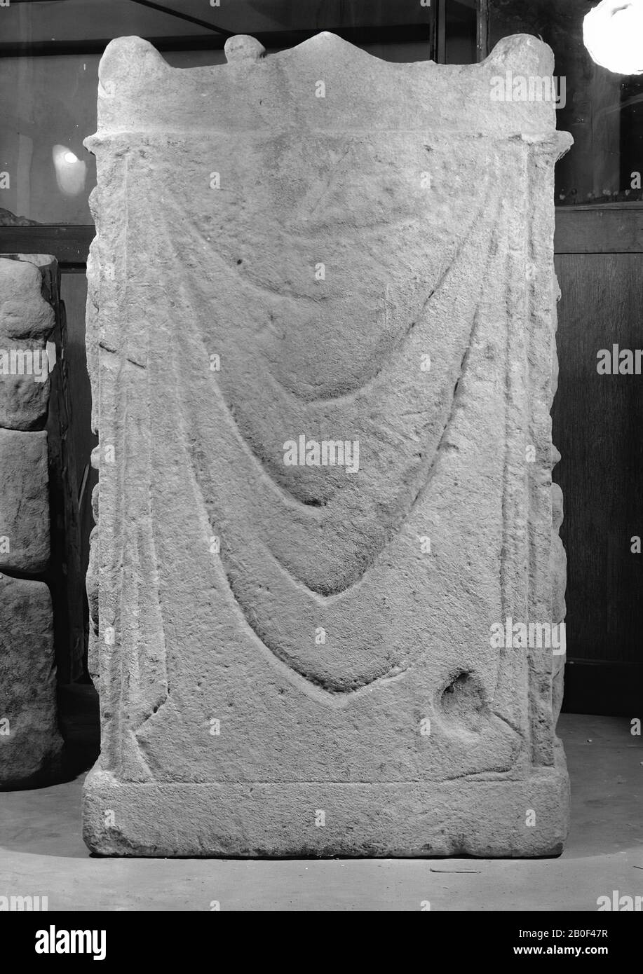 Altar with niche. Limestone. The architrave of the roof was supported by 2 detached, now demolished columns. Nehalennia sitting, with the right hand holding the rod of a ship's helm. Right side: at the top a woman with a garland (?) In the right hand, at the bottom a man with a jug (?) In the right hand. Left side: above a man with fruits on a leaf or shelf, at the bottom a man with a chest on the left shoulder. Rear decorated with curtain. On top originally four fruits, now still 1. The first line of the inscription is on the architrave., Altar, stone, limestone, 122.5 x 70 x 28 cm, roman 150 Stock Photo