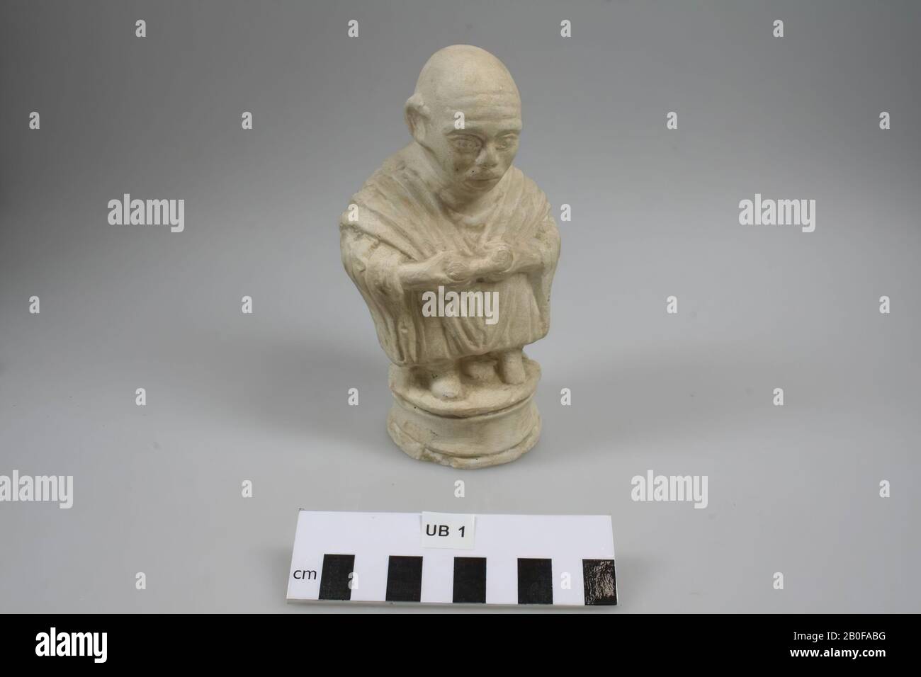 Casting of a terracotta statue of a bald-headed, standing dwarf wearing a Gallic coat and a cucullus with the hood backwards. He has a scroll in his hands., Casting, dwarf, plaster, 6,7 x 8,3 x 15,2 cm, roman, Netherlands, Utrecht, Bunnik, Fighting Stock Photo