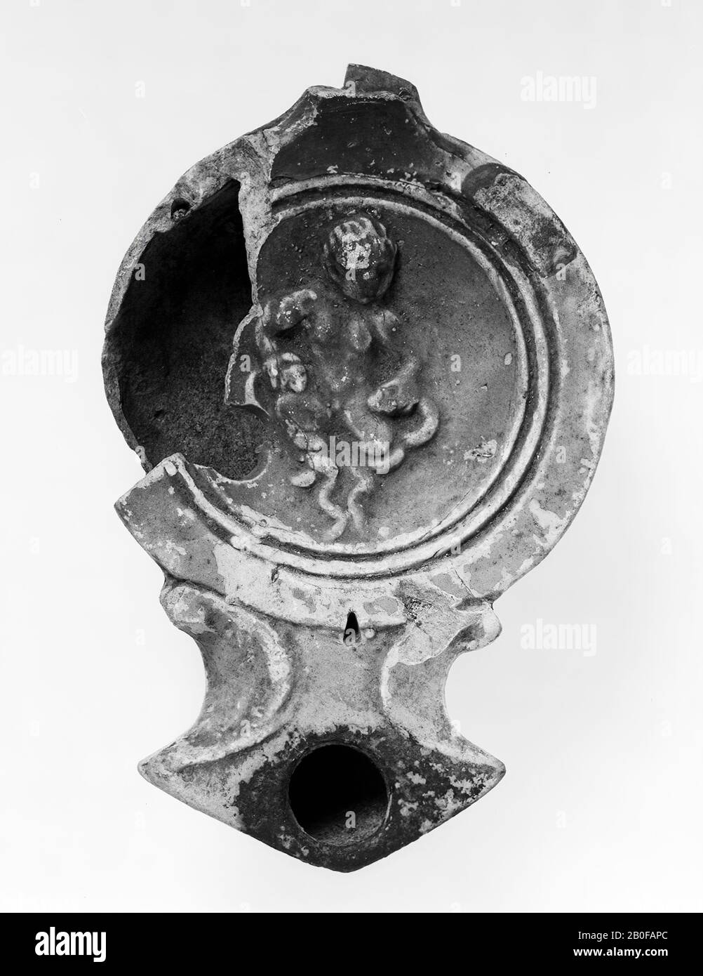 Earthen lamp with decorated mirror. Loeschcke type I C, shoulder form IVa.  Gray earth with yellowish-orange paint with dark spots. On the left side of  the mirror, a damage occurs over a