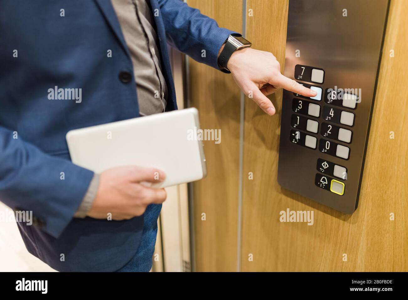 Man holding digital tablet while using elevator control panel. Stock Photo