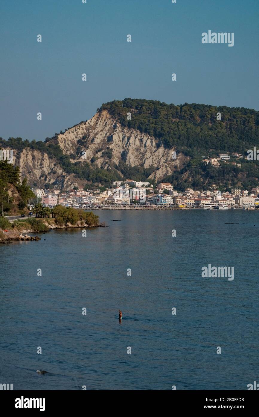 A long lens view of the port of Zakynthos town showing the buildings and harbour overlooked by the dominating limestone cliffs. Stock Photo