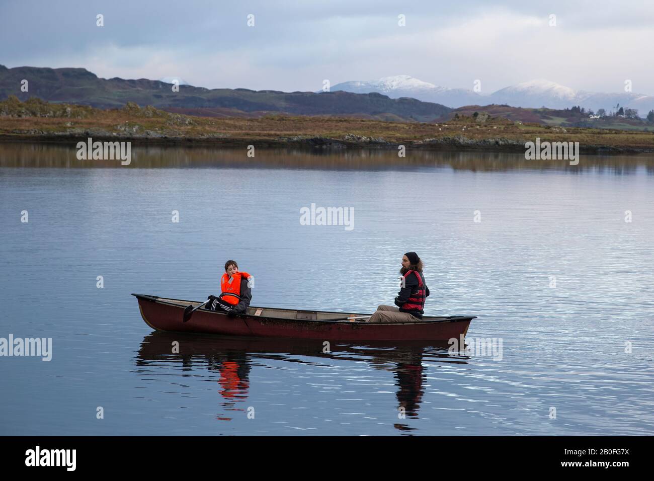 Father and son canoeing on the still waters of Ardmaddy bay on Christmas Day in West Scotland with snow capped mountains in the background Stock Photo