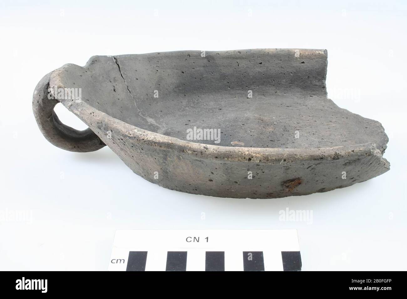 Oval dish (earthenware) of dark gray color, at one end still with an earpiece, the other end is broken. Rare form. Compare with urn C II 102. Old bonding, grease trap, earthenware (smooth wall), 6.5 x 24.8 x 16.9 cm, lme 1400-1600 AD, Netherlands, North Brabant, Cuijk, Cuijk Stock Photo