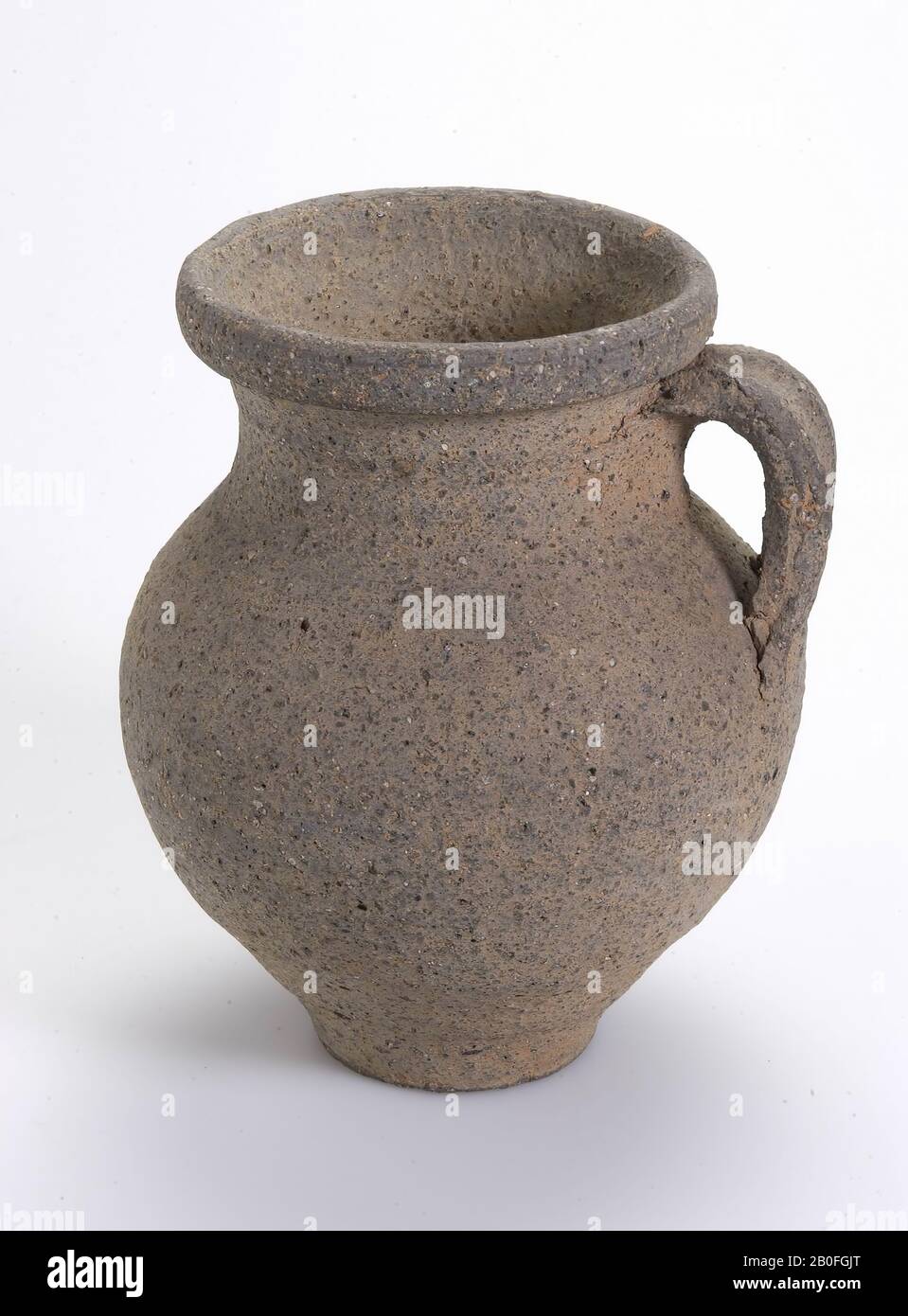 Gray rough-walled Frankish jug with ear. The cylinder neck, which is set off by a rib, passes unnoticed into the belly. Cool, jug, earthenware (Frankish), h: 13,9 cm, diam: 11 cm, vmeb 500-700 AD, Netherlands, Gelderland, Nijmegen, Nijmegen Stock Photo