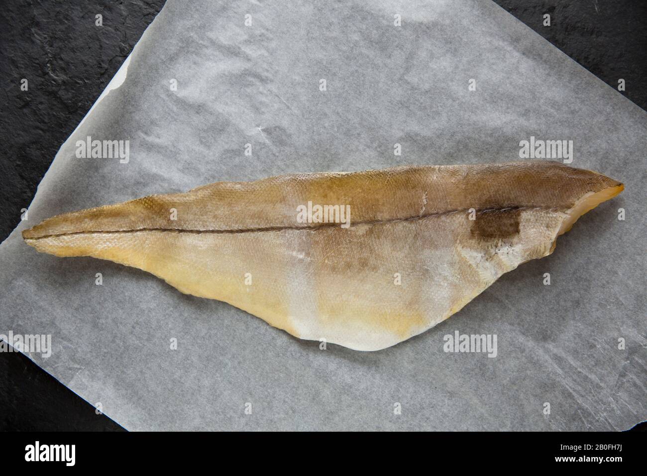 A smoked, undyed haddock fillet, Melanogrammus aeglefinus, bought from a supermarket fish counter in the UK and displayed on baking paper. It is photo Stock Photo