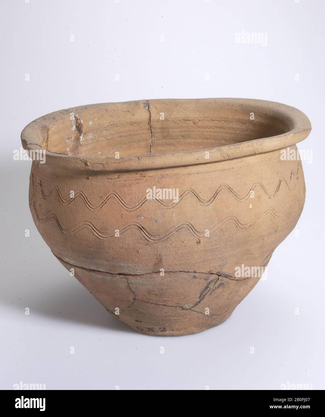 Pot or urn of baked earth, yellow-brown, on the thicker parts the inner has remained somewhat blackish, slightly rounded, round, without foot, from the bottom of the bottom. To the belly two wavy lines, grooved into the surface before baking. Broken but recovered again. Only bondings., Pot, cooking pot, earthenware (Frankish), h: 21.2 cm, diam: 29.1 cm, vmeb 400-500 AD, Netherlands, Gelderland, Barneveld, Garderen Stock Photo
