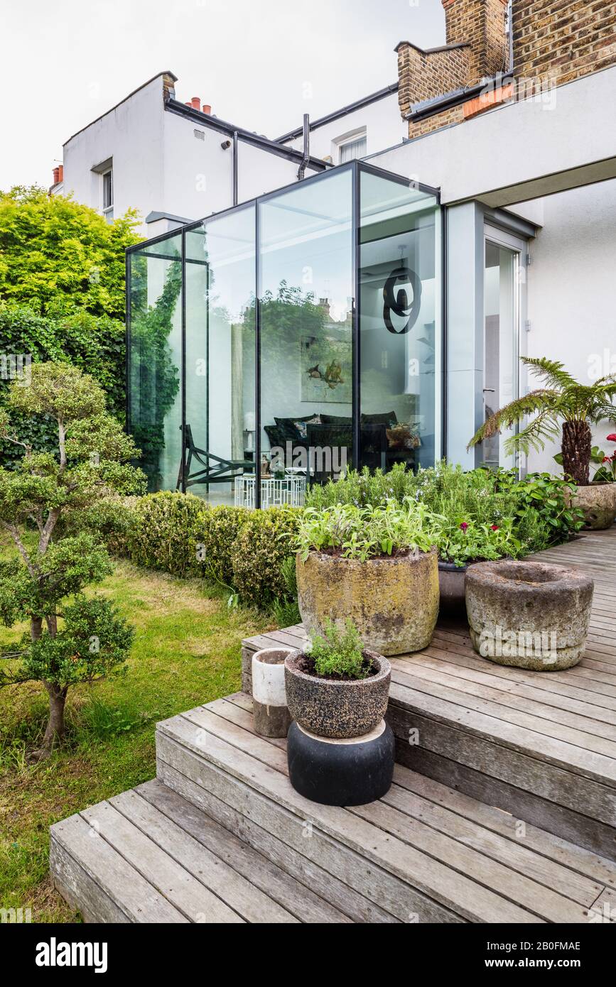 Pots and vintage planters on garden steps contrast contemporary glass box window. Stock Photo
