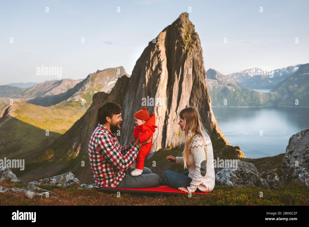 Travel family mother and father with baby outdoor camping healthy lifestyle Segla mountain view sustainable tourism in Norway man and woman with child Stock Photo