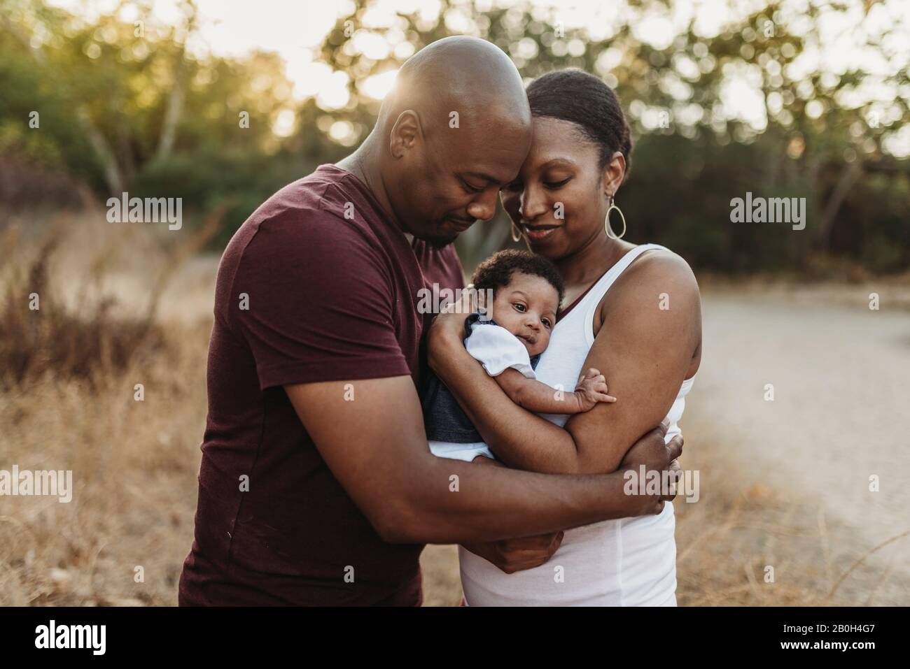 Close up happy mother and father cuddling infant girl backlit field Stock Photo