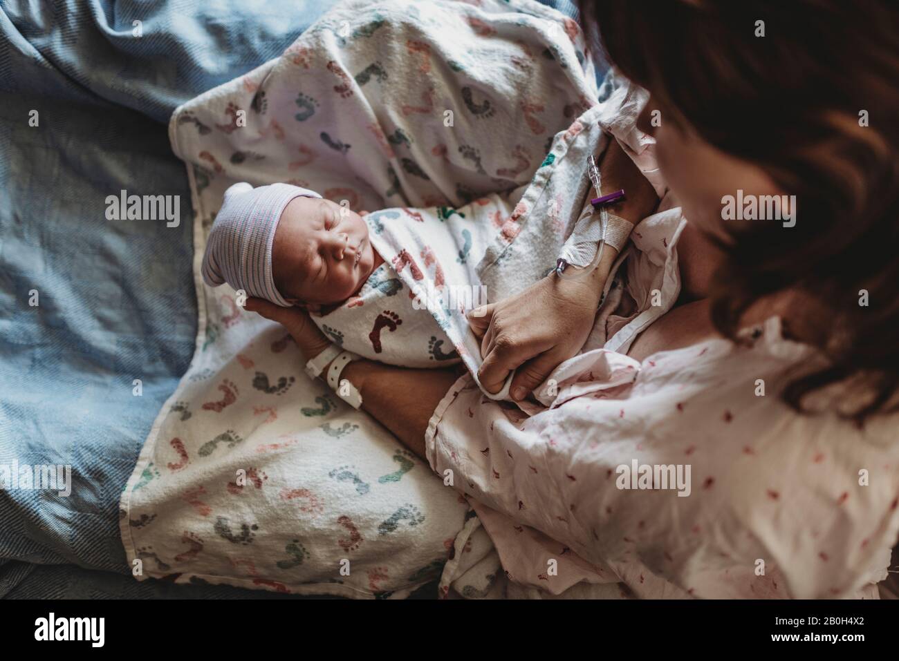 Overhead view of mother holding newborn boy with hat in hospital bed Stock Photo