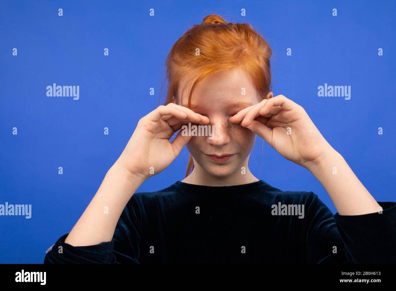girl rubs her eyes due to dryness on a blue background Stock Photo