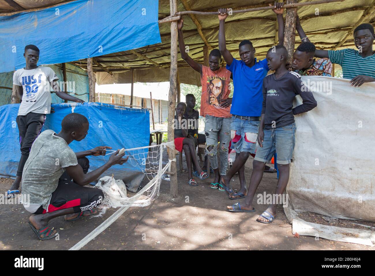 30.10.2019, Opanya, Gambela, Ethiopia - A man is tying a fishing net. Young men watch him do it. Fisheries project saving & credit group, livelihood. Stock Photo