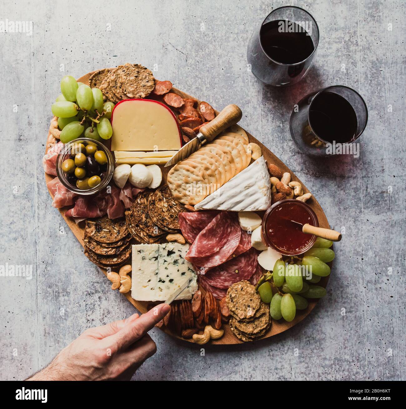Top view of hand cutting cheese on charcuterie board on stone counter. Stock Photo