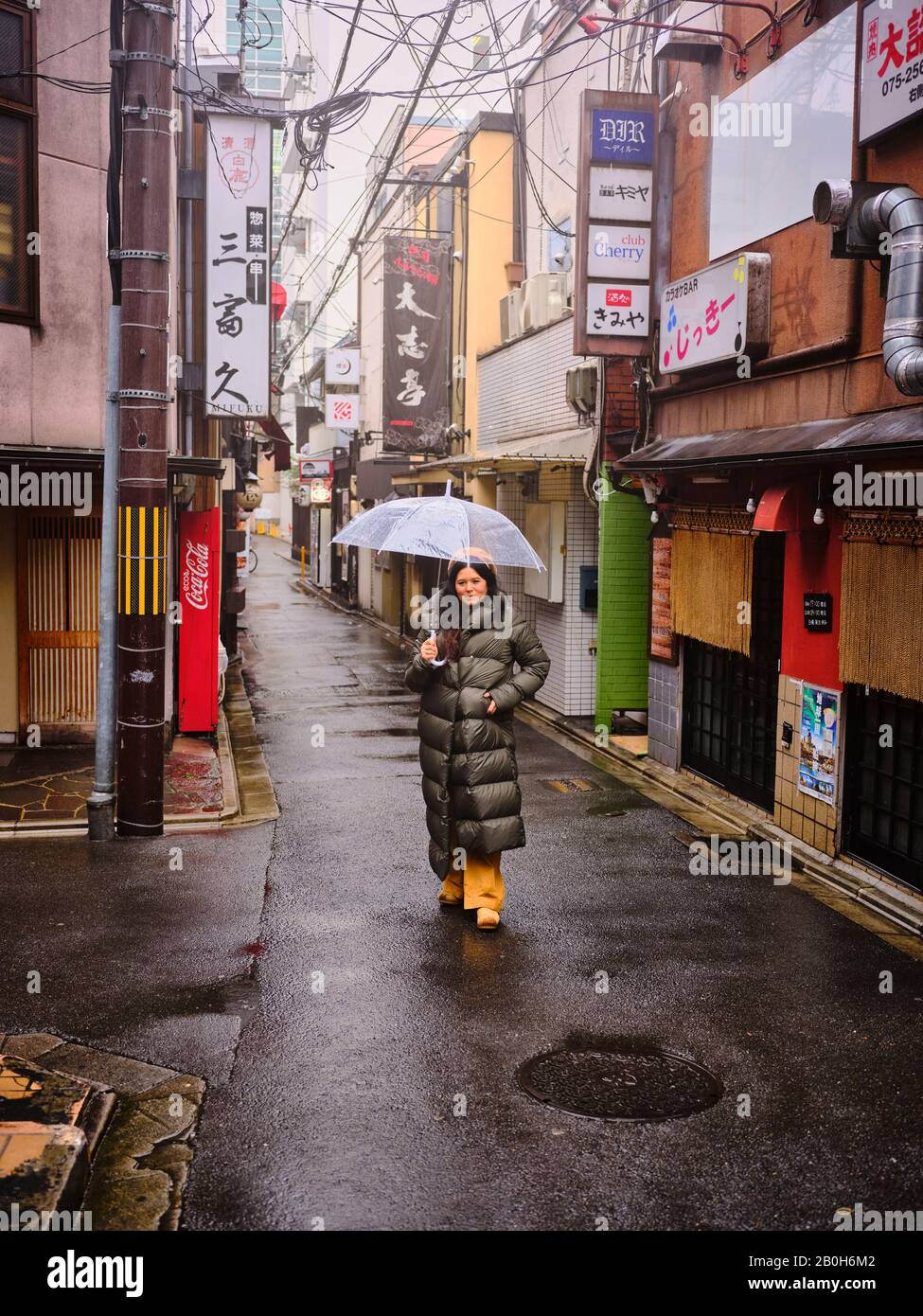 Woman in long rain jacket stands with umbrella in an alley Kyoto Japan Stock Photo