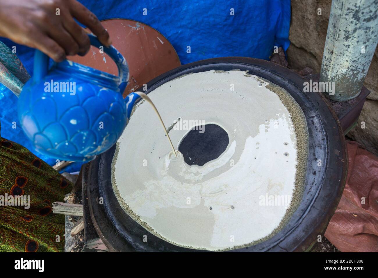 07.11.2019, Adama, Oromiyaa, Ethiopia - Production of the local sourdough bread Indjira. The liquid dough is poured onto a hot metal plate. Women and Stock Photo