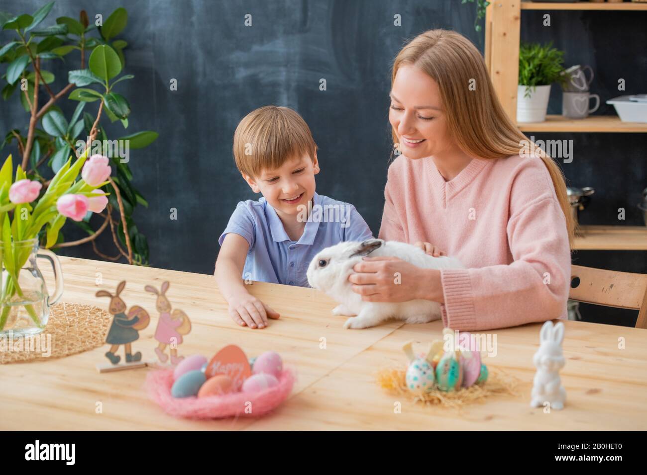 Smiling mother stroking fluffy rabbit together with excited son while celebrating Easter Stock Photo
