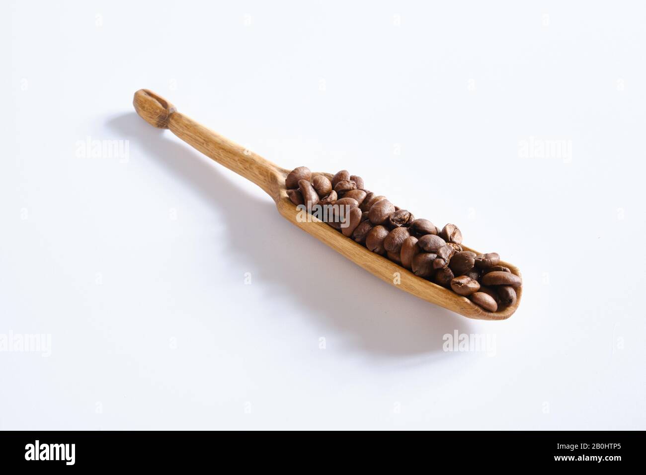 Handmade artisan  blackthorn wood coffee scoop spoon with bean detailing filled with coffee beans on handle white background Stock Photo