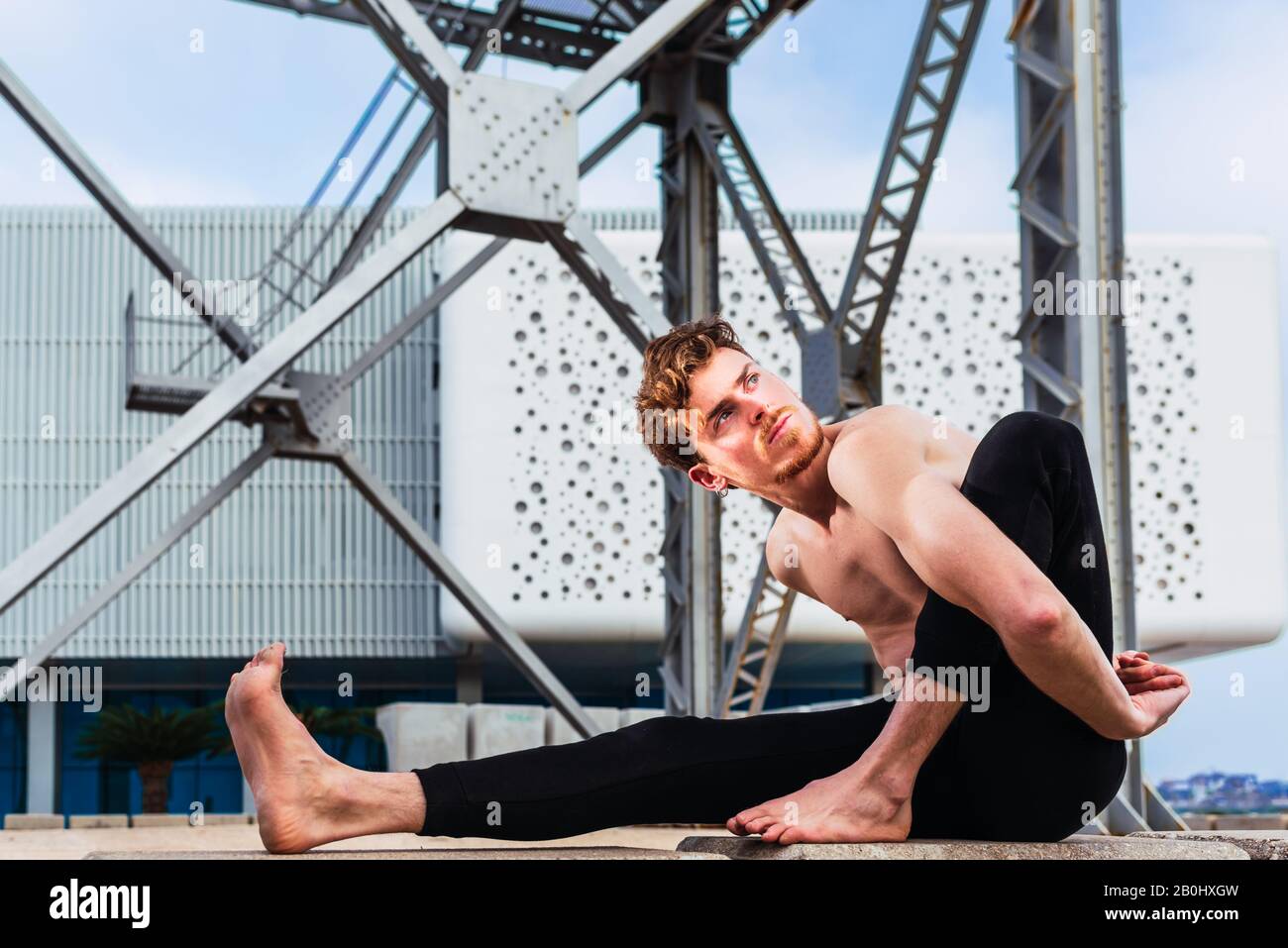 Young man  in the city in the yoga position ardha matsyendrasana stretching and relaxing her body and mind. Stock Photo