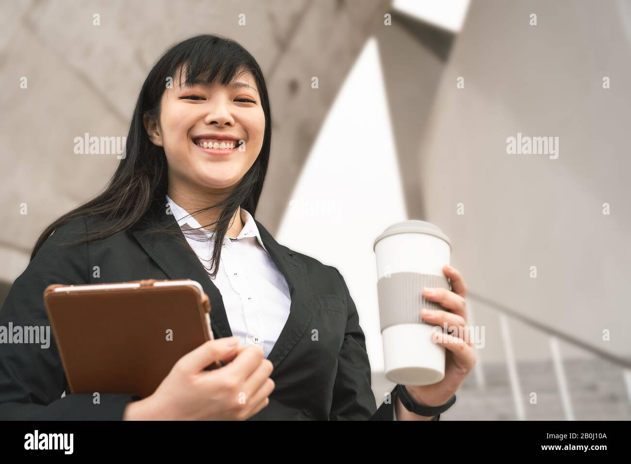 Business Asian woman holding laptop and coffee cup outdoor - Young smiling Chinese girl ready for working Stock Photo