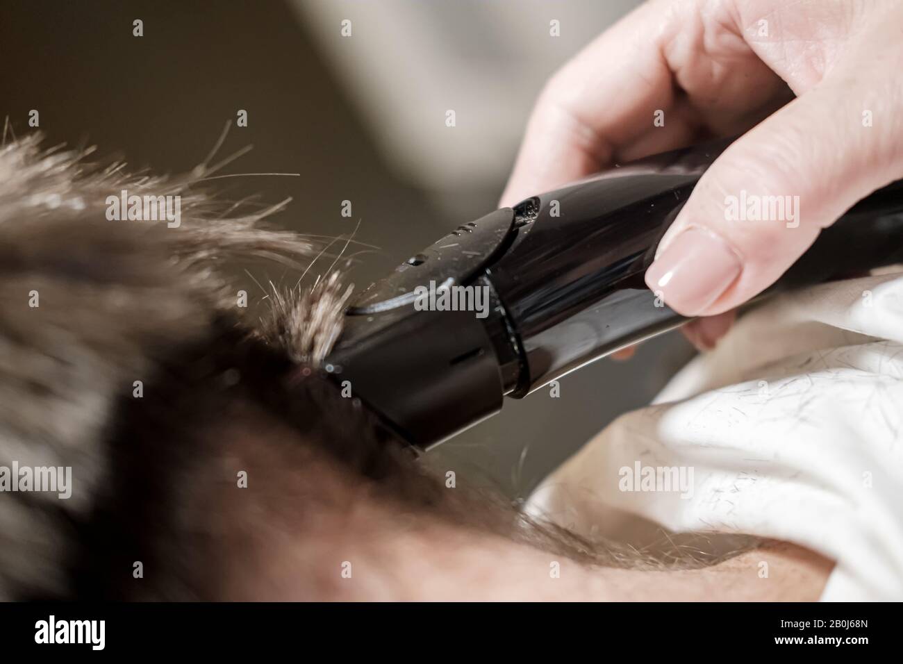 Female hand does cut hair on a mans head with a trimmer. Getting