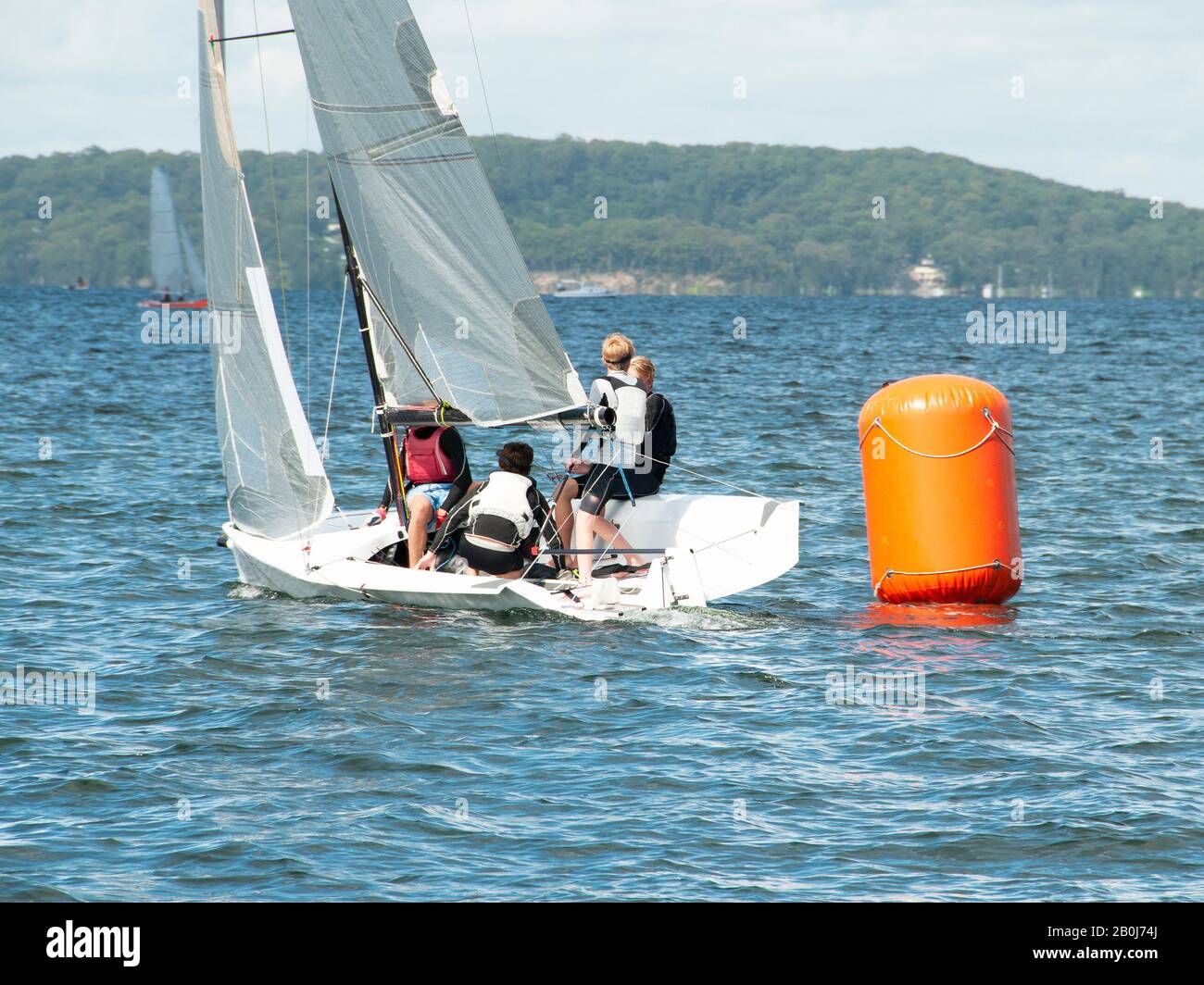 Young boys Racing small sailboat, rounding an orange marker. Teamwork by junior sailors racing on saltwater Lake Macquarie. Photo for commercial use. Stock Photo