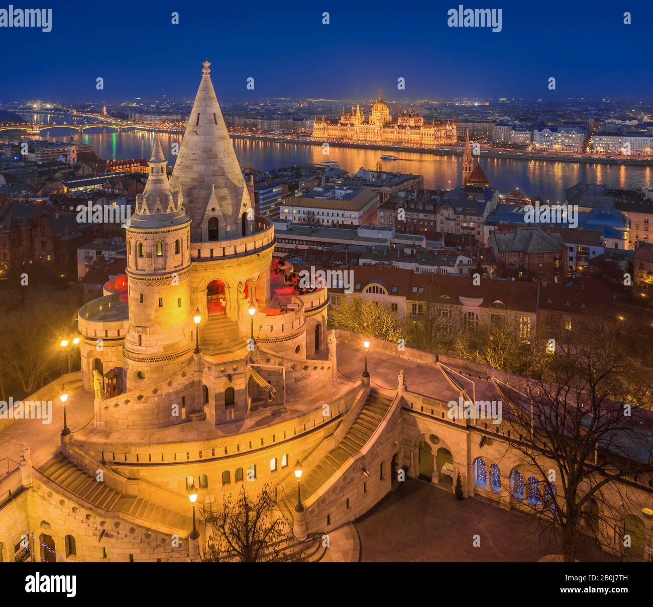 Budapest, Hungary - Aerial view of the main tower of Fisherman's Bastion (Halaszbastya) with illuminated Parliament of Hungary at blue hour on a winte Stock Photo