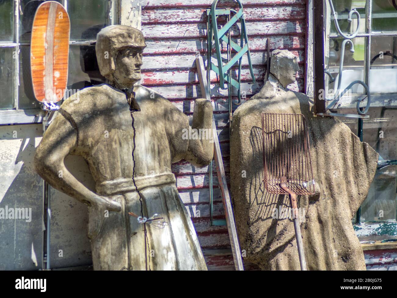 A pair of interesting statues stand guard outside an old wood barn in this fun salvage yard Stock Photo