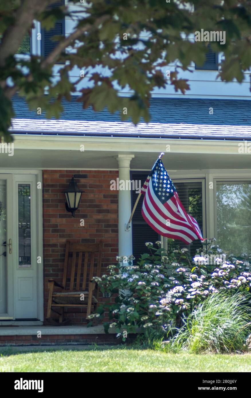 American flag blows in the breeze in this patriotic photo of a front porch in North America Stock Photo