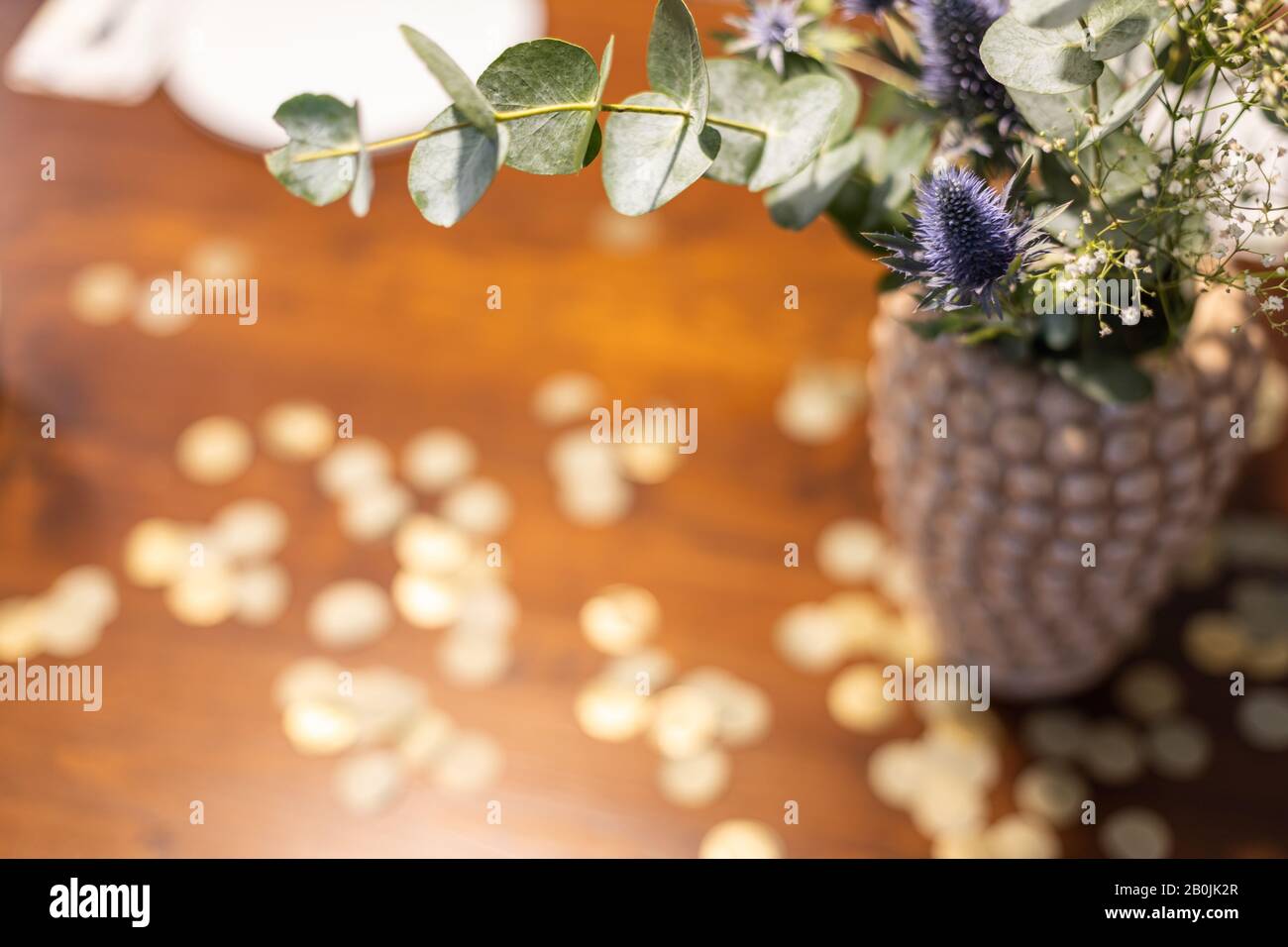 Vase with bouquet of flowers on a table with golden confetti. Stock Photo