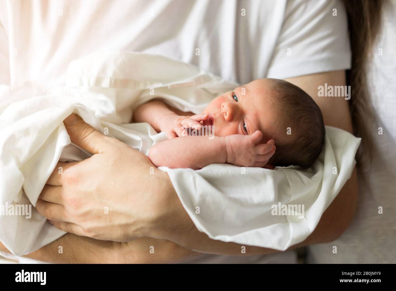 Father holds naked newborn son in his hands in a white diaper Stock Photo