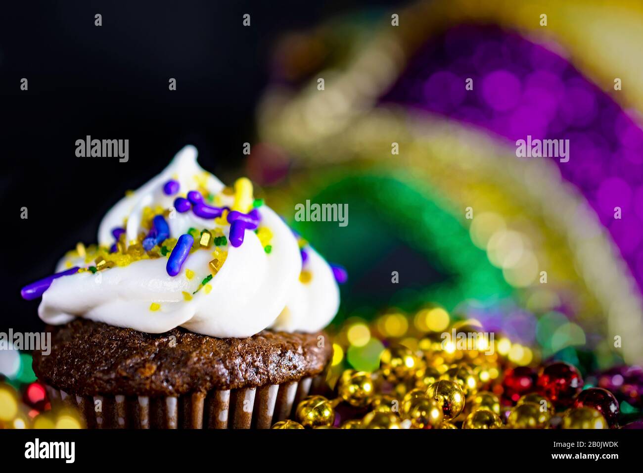 Extreme closeup of the top of a miniature cupcake with beads blurred in the foreground and a mask in the background.  Black background.  Shallow depth Stock Photo