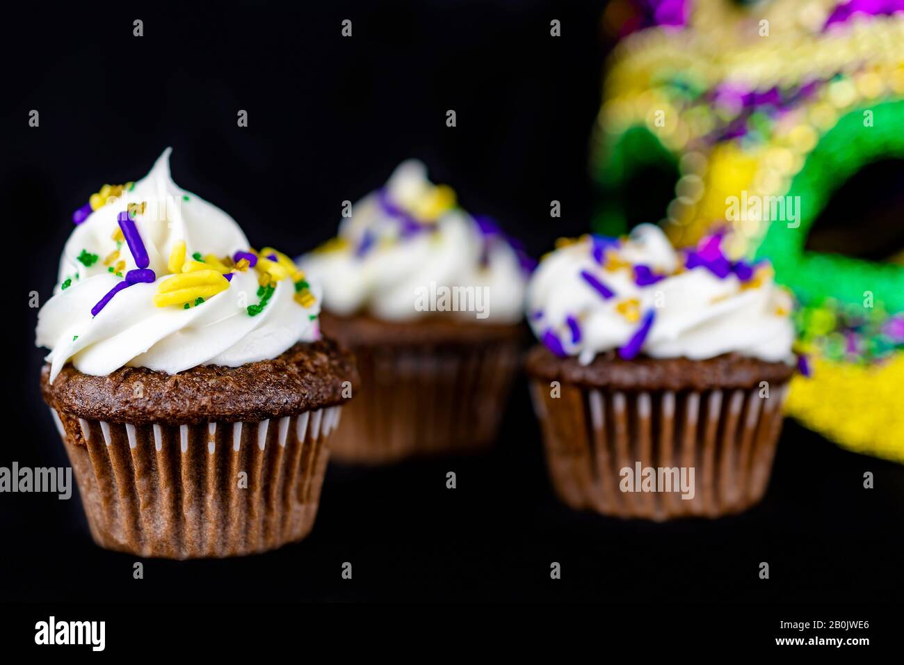 Three miniature cupcakes on a black background with a mask blurred in the background.  Shallow depth of field. Stock Photo