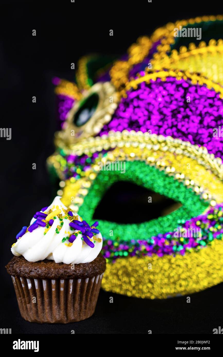 One miniature cupcake with a colorful mask in the background.  Black background. Stock Photo