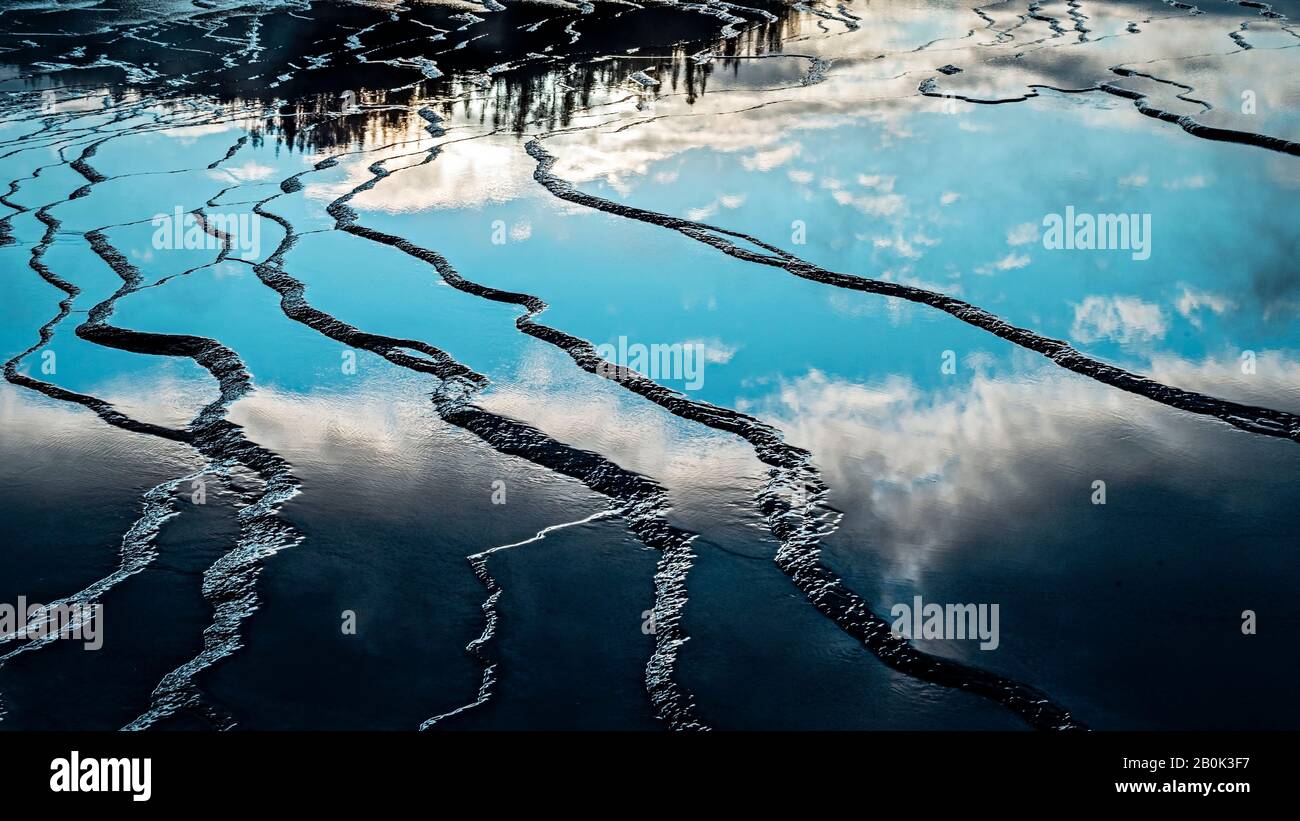 Wet layered flat rocky surface reflecting the blue sky and dark forest with mirror like quality. Stock Photo