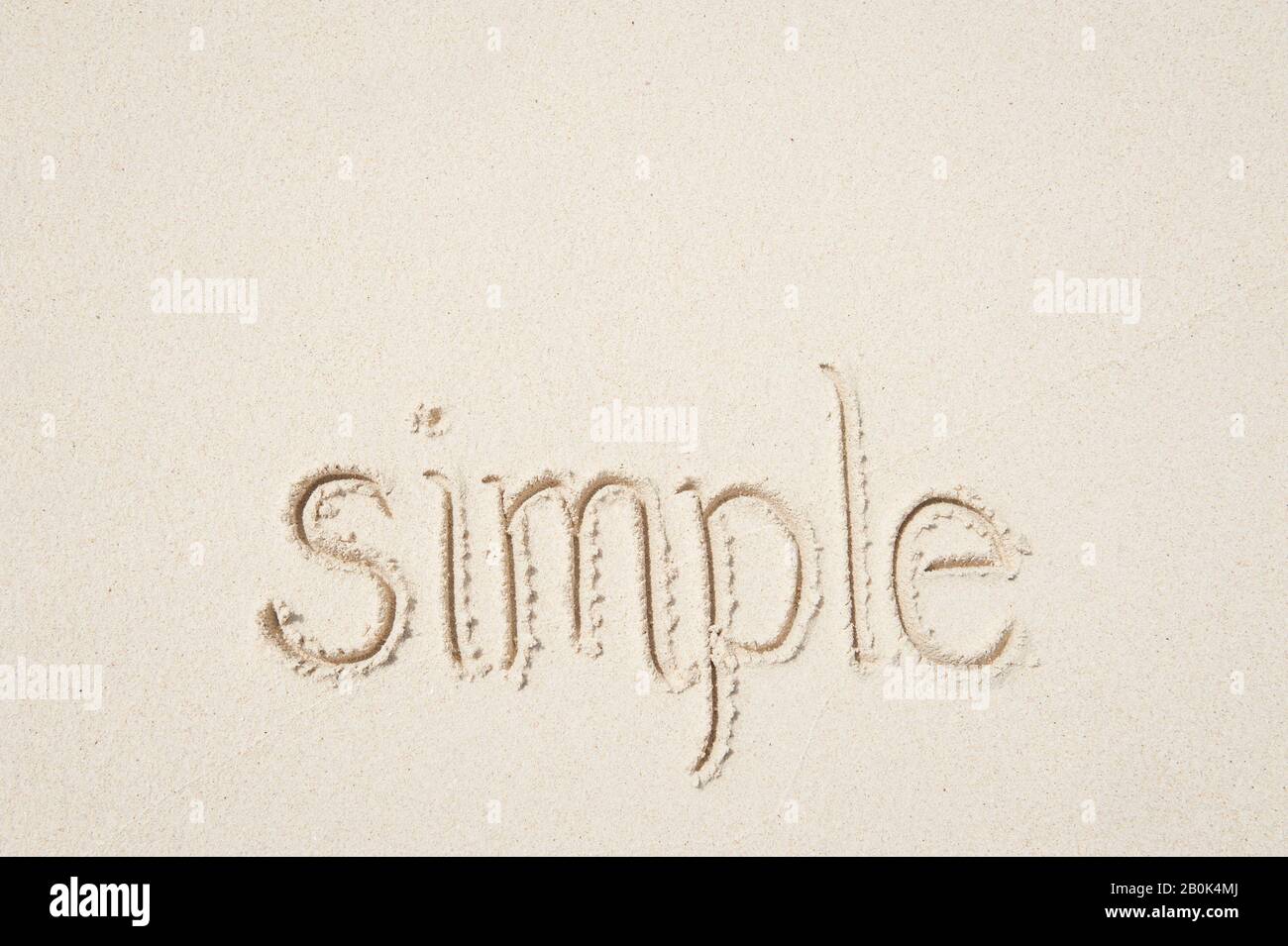 Simple message of simplicity handwritten outdoors on clean smooth sand beach Stock Photo