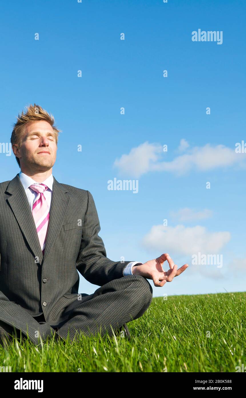 Meditating businessman sitting with eyes closed in a cross-legged yoga ...